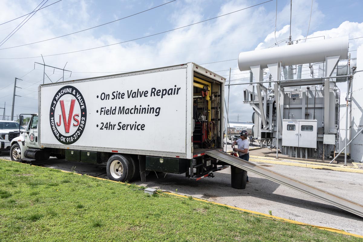 A service truck labeled On Site Valve Repair, Field Machining, 24hr Service is parked near industrial equipment. The trucks rear is open with a ramp extended, and a worker stands nearby.