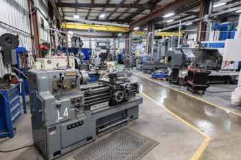 A spacious industrial workshop with several large metalworking machines, including lathes and milling equipment. The area has concrete floors, overhead lighting, and various tools and parts organized throughout the space. A spacious industrial workshop with several large metalworking machines, including lathes and milling equipment. The area has concrete floors, overhead lighting, and various tools and parts organized throughout the space.