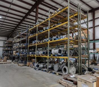 Large warehouse with tall metal shelves stocked with various industrial metal pipes, fittings, and equipment. Some items are on pallets; the concrete floor is clear, and the ceiling has exposed beams and lights. Large warehouse with tall metal shelves stocked with various industrial metal pipes, fittings, and equipment. Some items are on pallets; the concrete floor is clear, and the ceiling has exposed beams and lights.